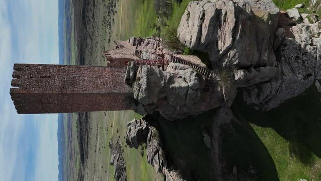 Approaching drone aerial view, vertical mode, to the main tower of a medieval castle built in the top of a rocky hill.  Guadalajara, Spain.