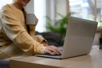 Young woman holding cup of coffee and using laptop in living room