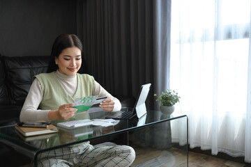 Millennial woman holding account passbook and credit card, calculating expenses at home