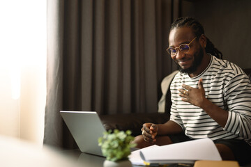 Smiling young African man freelancer having video call on laptop during working at home