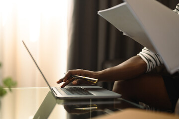 Cropped shot African millennial man freelancer sitting on couch and working with laptop