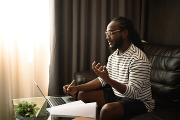 Smiling young African man freelancer having video call on laptop during working at home