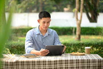 Portrait of young businessman in smart casual wears using digital tablet at outdoor cafe