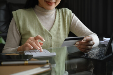 Cropped shot young woman holding credit card and calculating expenses at home