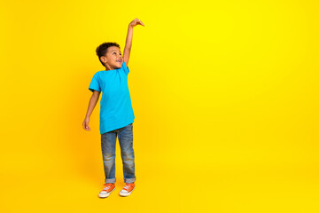 Full length photo of good mood child with curly hair dressed blue t-shirt look empty space show height isolated on yellow background - obrazy, fototapety, plakaty