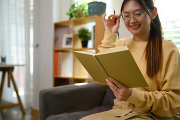 Pretty young woman listening to music with headphone and reading book at home