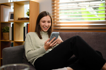 Relaxed caucasian woman sitting on couch at home and using mobile phone