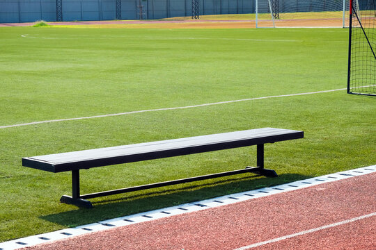 Empty bench on the sports field with green grass and red running track