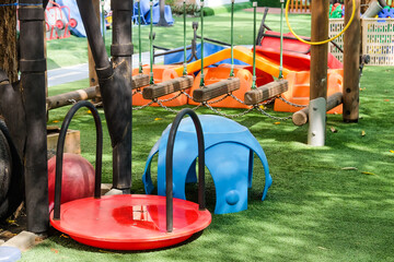 Playground in the park with blue and red seats and swings.