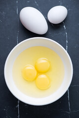 Raw goose and chicken eggs on a black marble background, vertical shot, top view