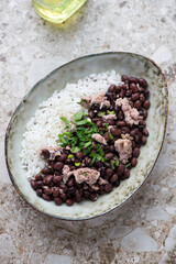 Oval bowl with black beans and rice on a light-brown granite background, vertical shot, elevated view