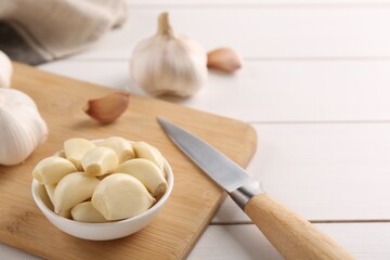 Fototapeta na wymiar Fresh garlic and knife on white wooden table, closeup. Space for text