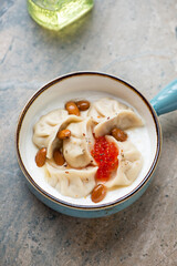 Vareniki or dumplings served with yogurt and red caviar in a turquoise bowl, vertical shot on a light-brown granite background