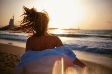 Woman gazes towards the sea with wind blowing her hair, with the Burj Al Arab in the distance