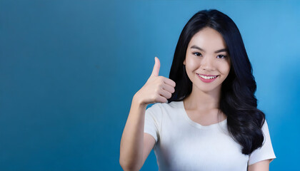 Portrait of a smiling happy woman with thumbs-up hand gesture on blue background. Approval gesture.