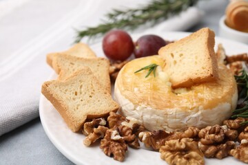 Tasty baked camembert, croutons and walnuts on table, closeup