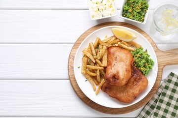 Tasty fish, chips, sauce, peas and lemon on white wooden table, top view. Space for text