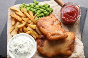 Tasty fish, chips, sauces and peas on grey table, above view