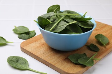 Fresh spinach leaves in bowl on white tiled table, closeup