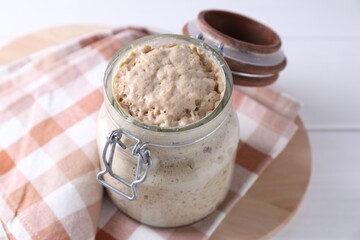Sourdough starter in glass jar on white wooden table, closeup