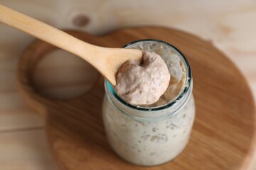 Taking sourdough starter with spoon at table, closeup