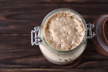 Sourdough starter in glass jar on wooden table, top view. Space for text