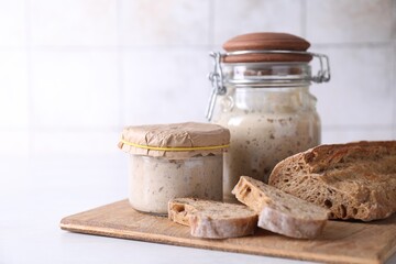 Sourdough starter in glass jars and fresh bread on light table. Space for text