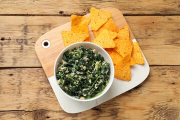 Tasty spinach dip with eggs in bowl and nachos chips on wooden table, top view