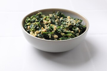 Tasty spinach dip with egg in bowl on white table, closeup