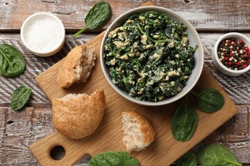 Tasty spinach dip with egg in bowl, bread and spices on wooden table, top view