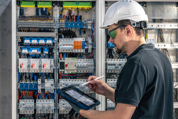 Man, an electrical working in a switchboard with fuses, uses a tablet. - 786050160