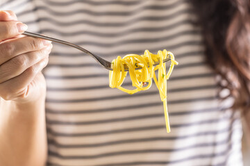 Young woman enjoys eating spaghetti. He has Aglio e Olio pasta twisted on his fork. - 786064919