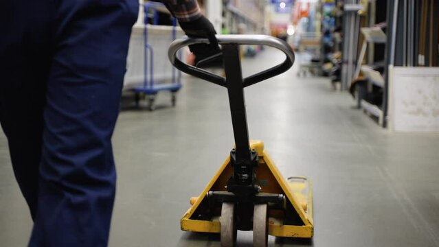 A worker in a warehouse or hardware store uses a hand pallet stacker to transport pallets