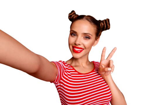 Young woman with funky mood making v-sign and selfie on the front camera of smartphone, playful and happy isolated on red background