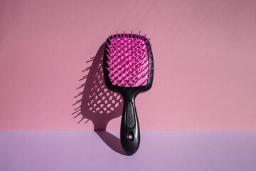Hairbrush leaning against wall, bathed in sunlight, casting bold shadow. Pink and violet color...