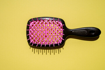 Top view of a hair brush on a vibrant yellow surface, showcasing neon pink and black colors with...