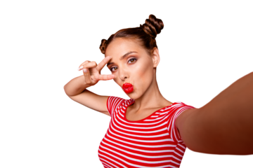Pretty cheerful girl with pouted lips shooting selfie and holding two fingers near eyes showing v-sign isolated on red background