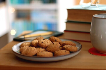 Cup of tea or coffee, pile of books, plate of cookies, reading glasses, e-reader and pen on the...