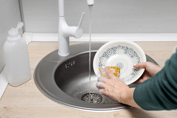  housewife washes a plate in the kitchen sink.