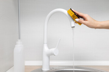housewife wiping a kitchen faucet with a sponge