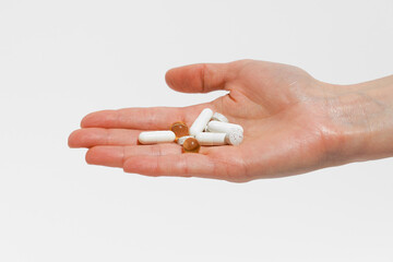 Female hand holding white pills and capsules on white isolated background. The concept of health care, pharmacy and dietary supplements for the treatment of diseases.
