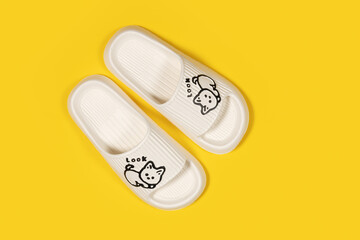 A pair of beige rubber slippers with cat on a yellow background. Fashionable rubber slippers