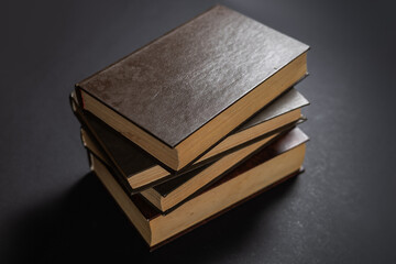 Vintage, antiquarian books pile on wooden surface in warm directional light. Selective focus