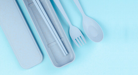 Plastic spoon and fork with container on blue background.