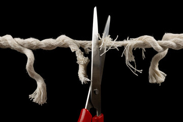 Worn rope ready to break, with scissors on black background.