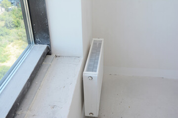 Top view on  house metal radiator heating and unfinished window sill with plastering walls.