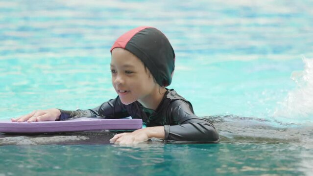 A Thai Asian kid girl, aged 8 to 10 years, has a cute face and a cheerful smile. She is playing and exercising by playing in the swimming pool. Swimming makes the body strong and healthy.
