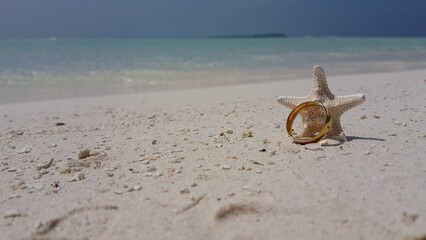 Closeup shot of a golden ring and a starfish on the sand in the Maldives