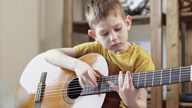 A cute cheerful boy is playing classical guitar in the children's room. The child learns to play musical instruments
