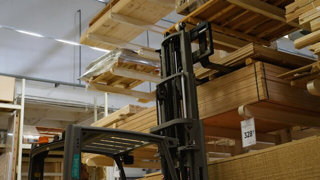 Warehouse worker driver in uniform loading lumber by forklift stacker loader